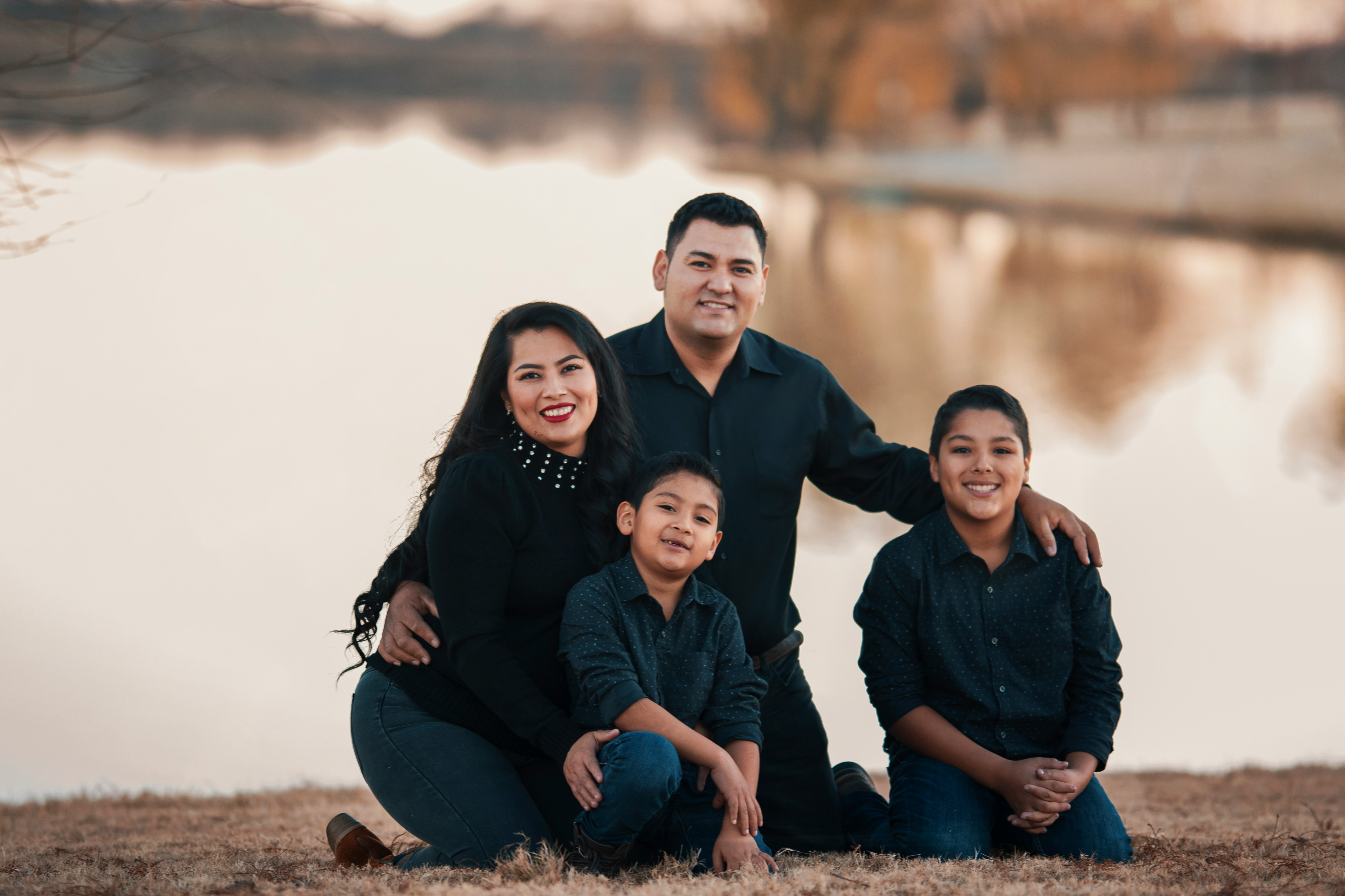 A family of four kneeling beside a body of water