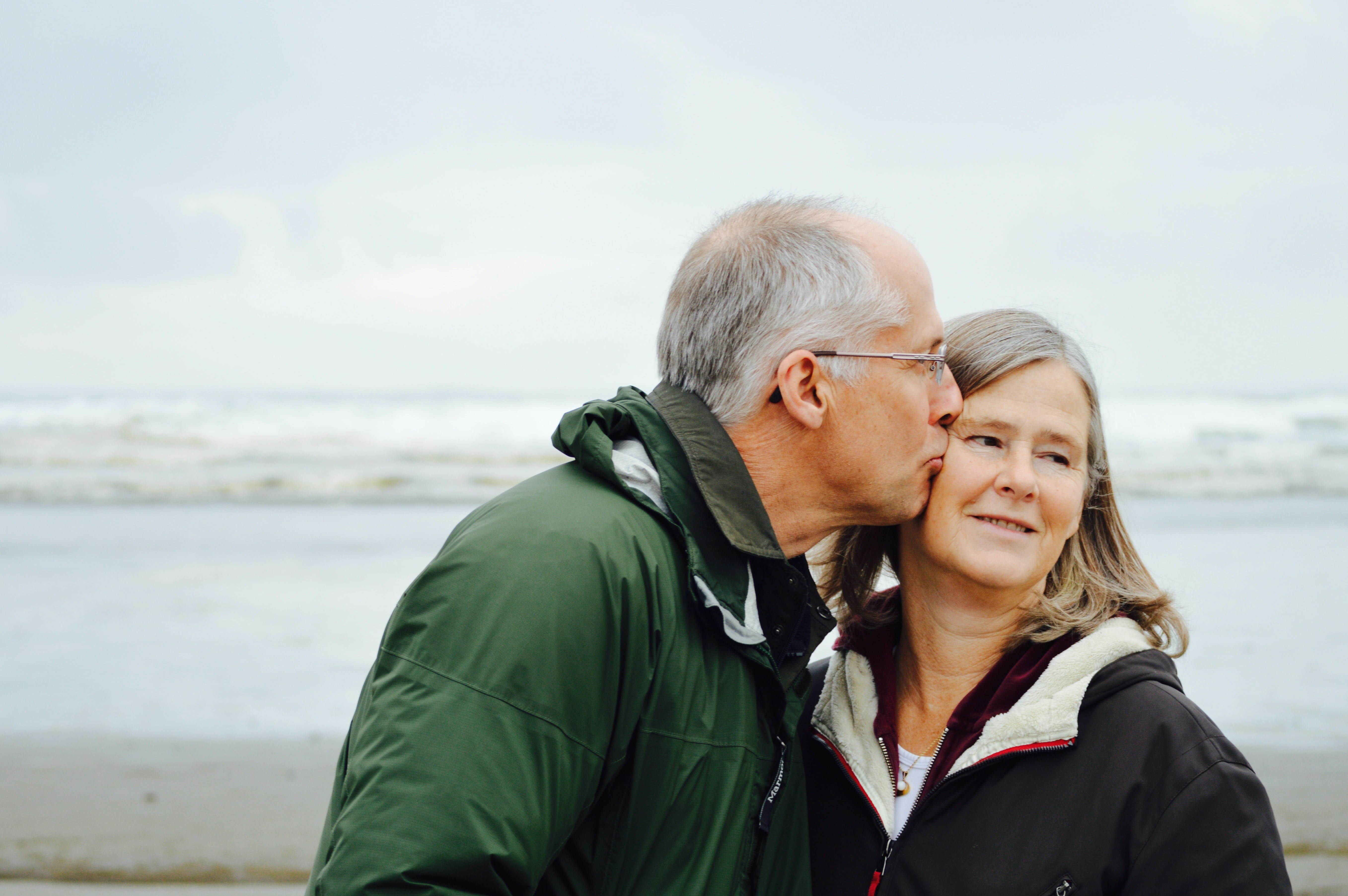 Older couple at the beach man kissing woman on cheek