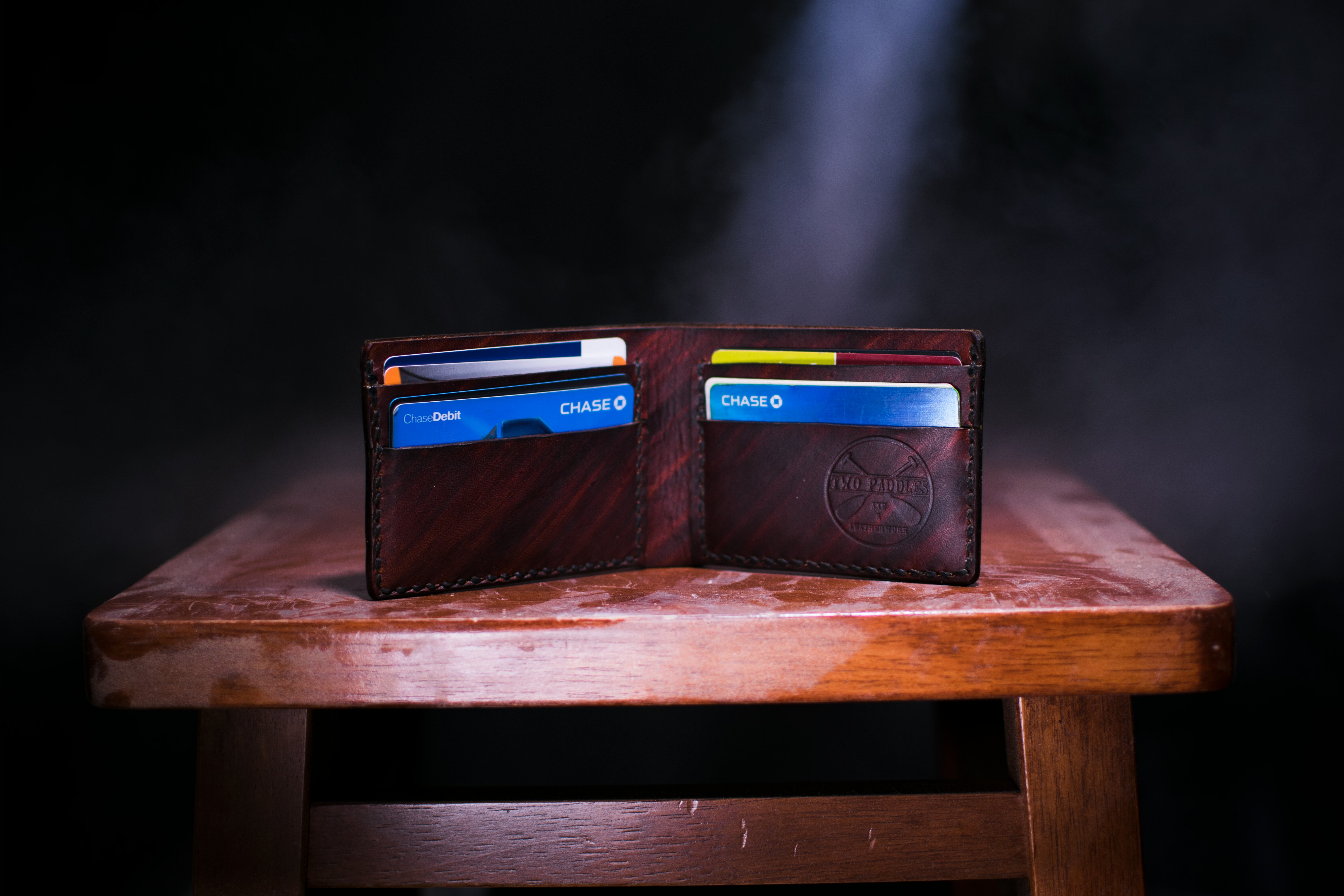 Brown bifold leather wallet carrying several credit cards standing on a wooden stool