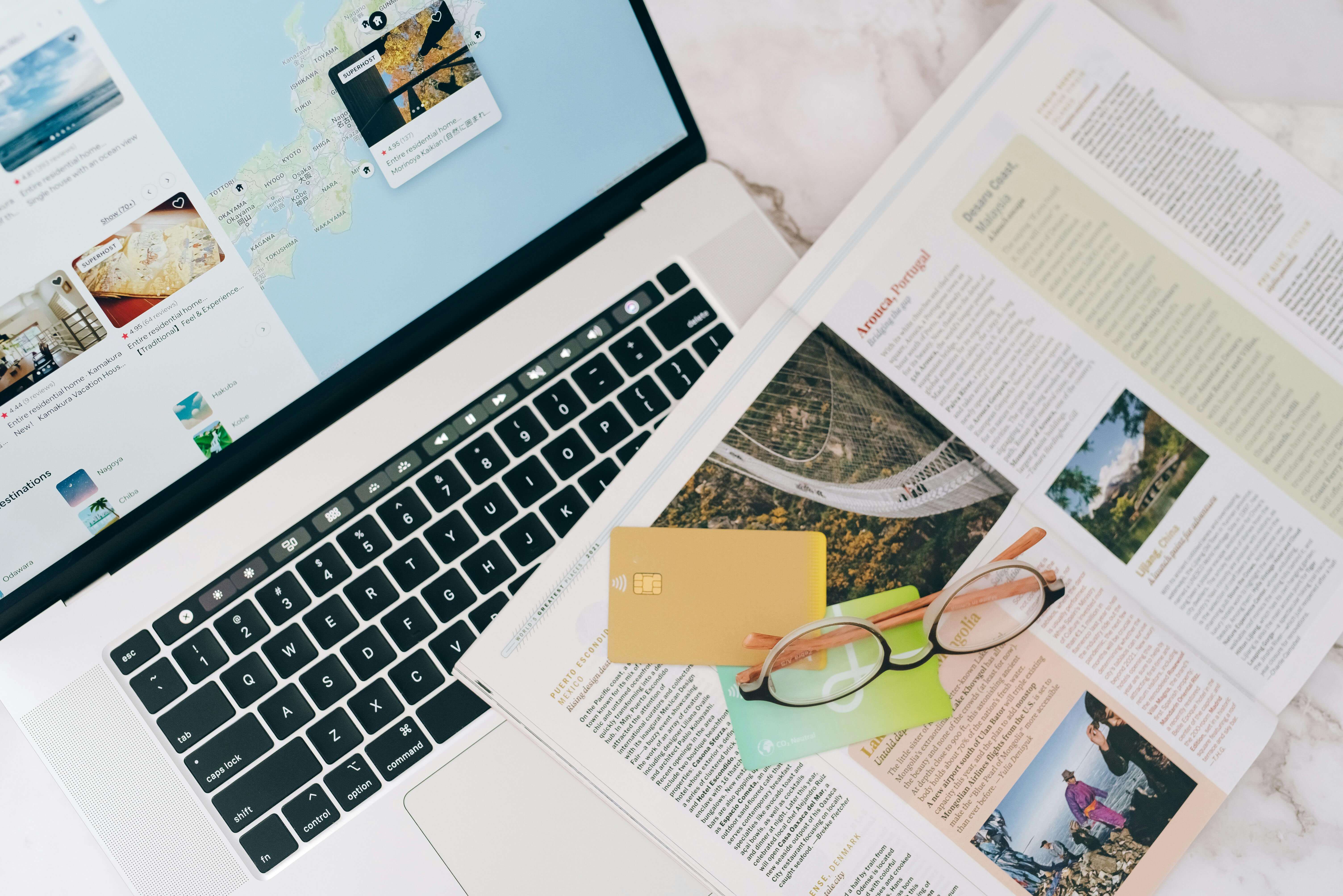 Credit cards and travel magazine on top of a laptop computer