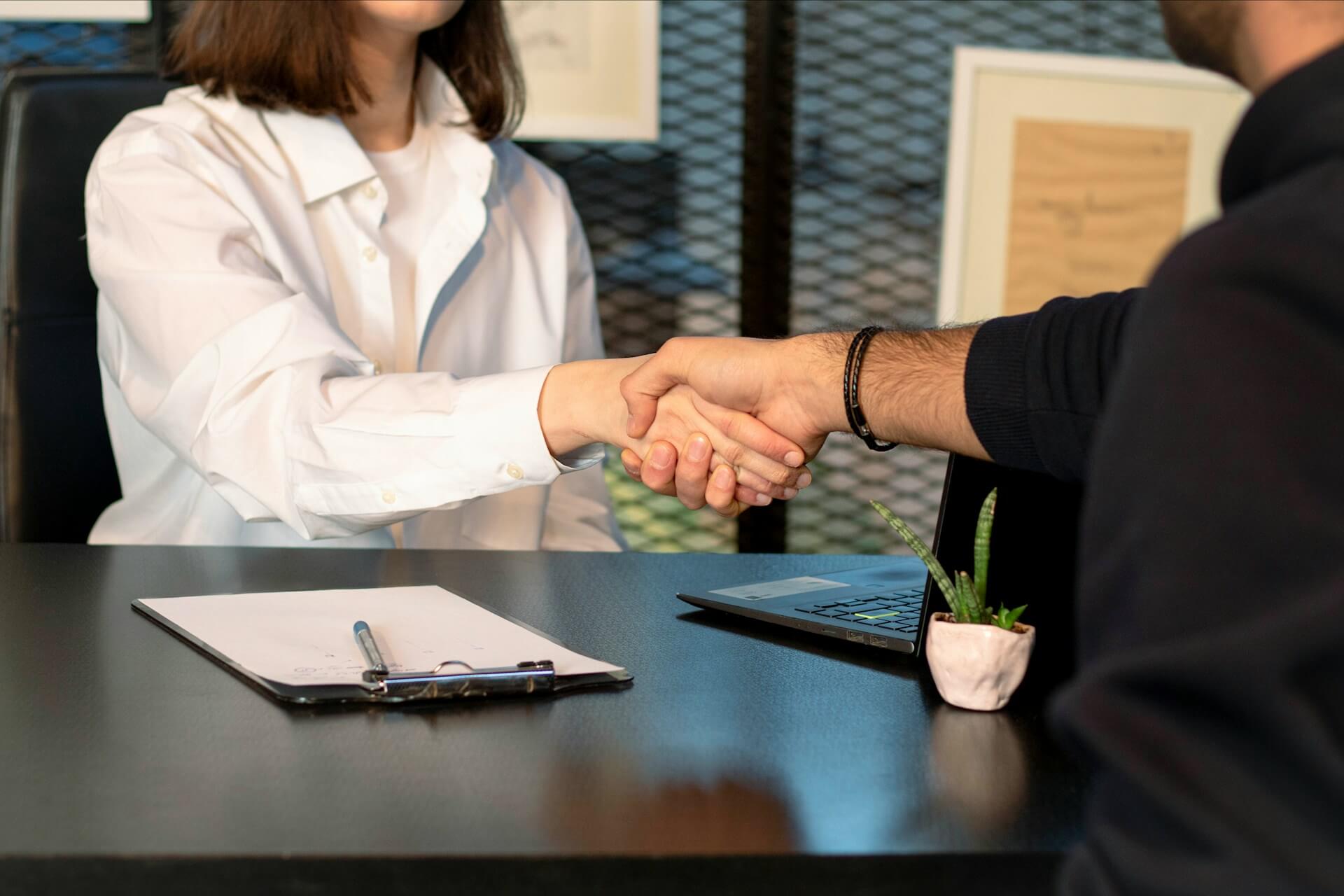 A man and a woman seated shaking hands after entering into a contract .