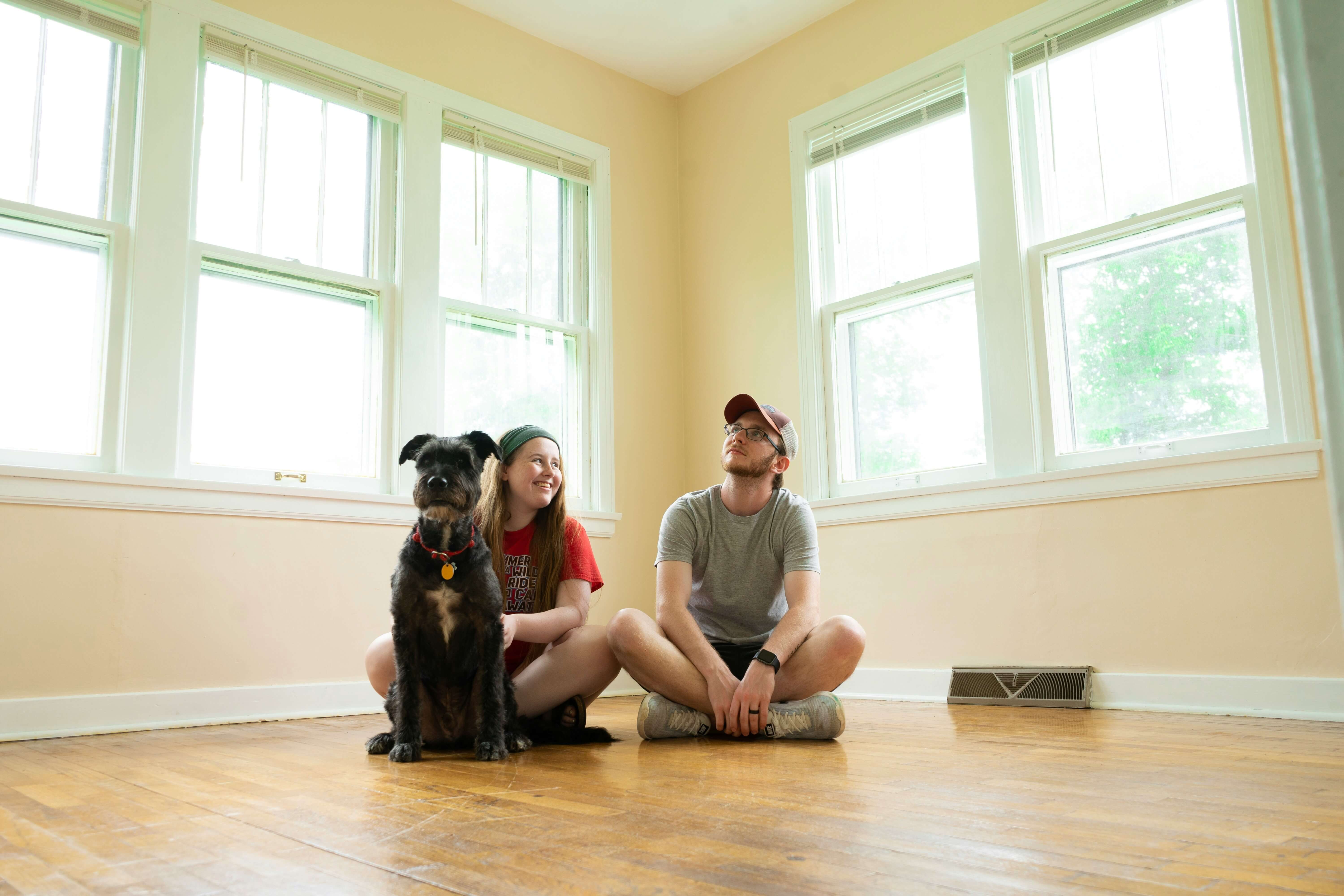 Man, woman, and dog sitting on the wooden floor of an empty house