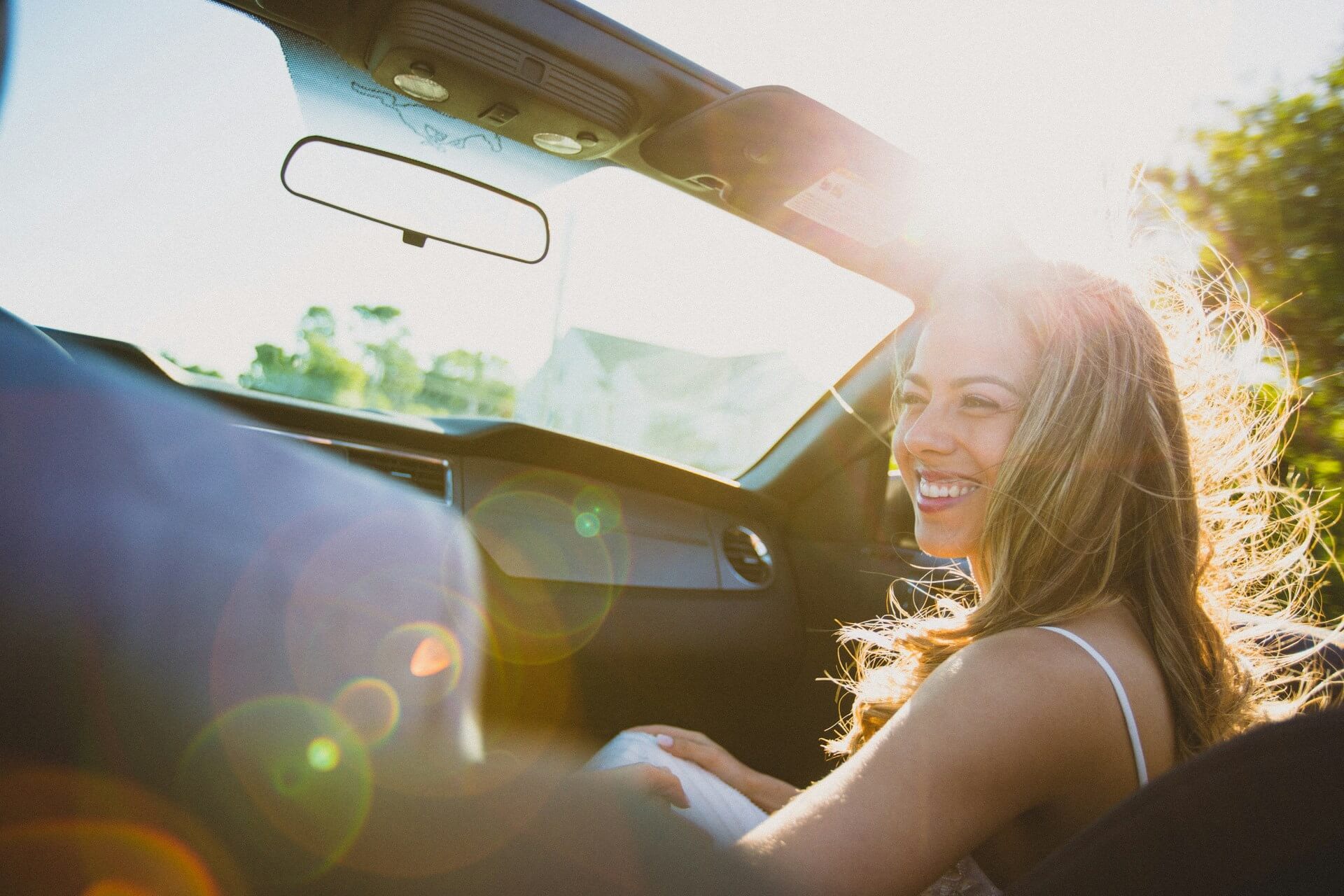 Smiling woman sitting inside a vehicle with the sun shining down