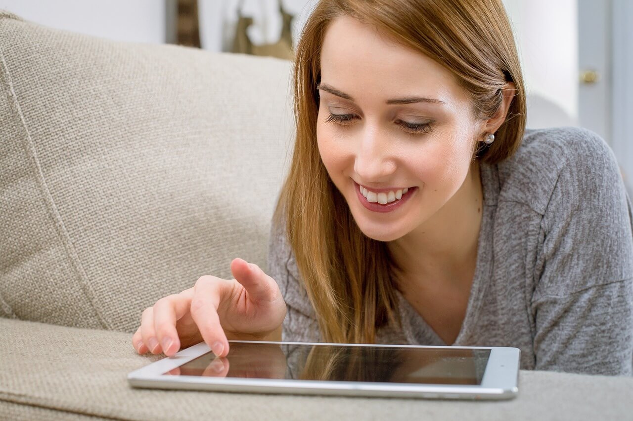 Woman lying on a couch using a tablet.